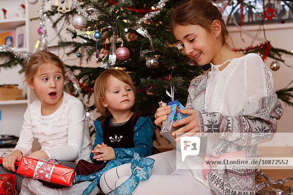 Mädchen vor dem Weihnachtsbaum beim Öffnen von Geschenken