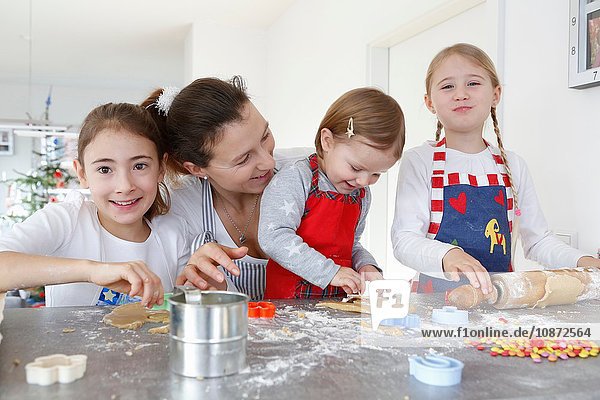 Girls with mother at kitchen counter making cookies smiling