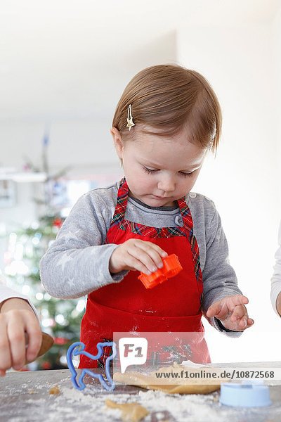 Girl wearing apron looking down using cookie cutter
