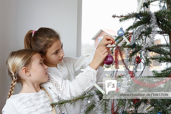 Seitenansicht von Mädchen  die den Weihnachtsbaum mit Christbaumkugeln schmücken
