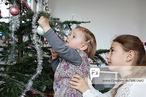 Side view of big sister helping girl decorate christmas tree