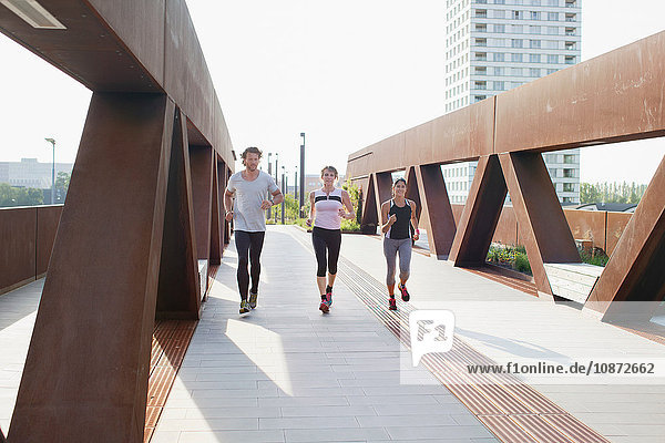 Male and female runners running on urban footbridge