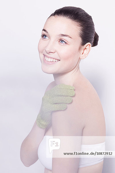 Kopf- und Schulteraufnahme einer schönen jungen Frau  die mit einem grünen Massagehandschuh die Schulter massiert