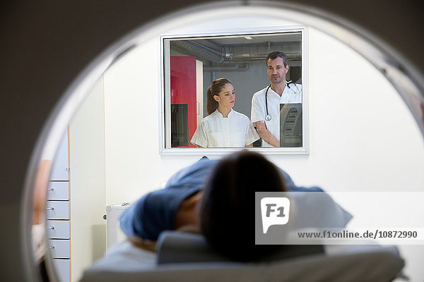 Arzt und Krankenschwester beobachten weibliche CT-Patientin vom Fenster des Kontrollraums