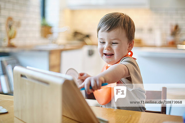 Kleiner Junge sitzt am Tisch und zeigt auf ein digitales Tablett