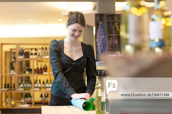 Verkäuferin im Weinladen wickelt Weinflasche in Seidenpapier ein