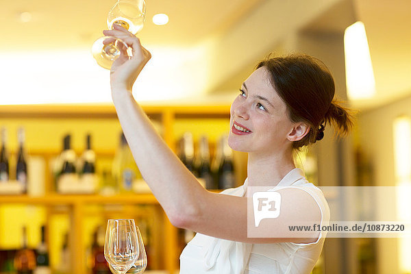 Frau im Weinladen hält Weinglas hoch und kontrolliert die Sauberkeit