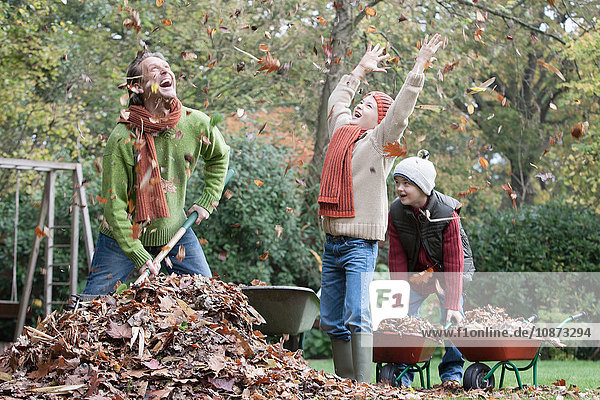 Father and sons fooling around in garden  gathering autumn leaves