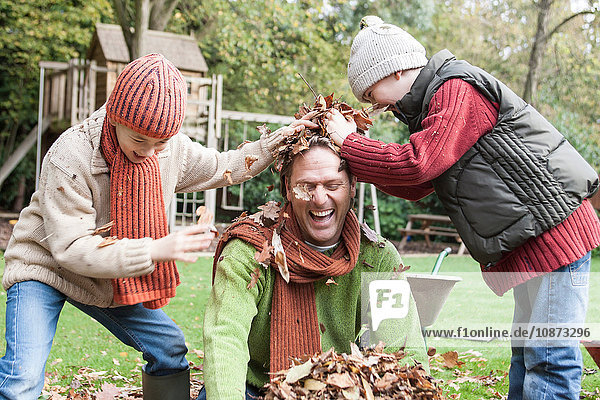Vater und Söhne treiben sich im Garten herum und werfen Herbstblätter
