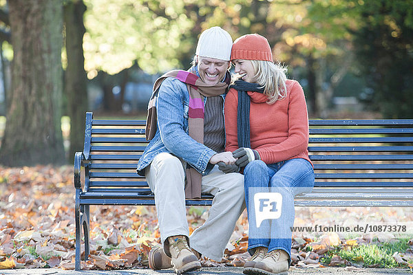Heterosexuelles Paar sitzt zusammen auf einer Parkbank  hält Händchen und lacht