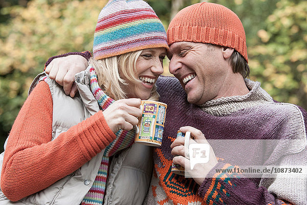 Heterosexual couple outdoors  holding hot drinks  smiling
