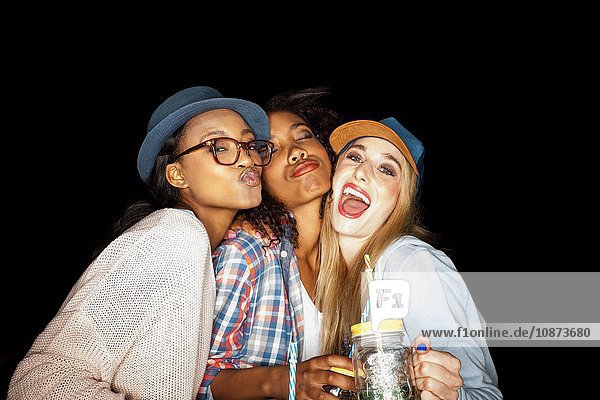 Young women huddled together holding mason jars looking at camera puckering lips
