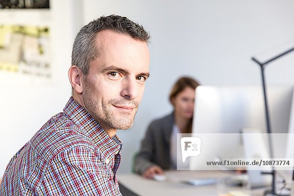 Side view of mature man in office looking at camera smiling