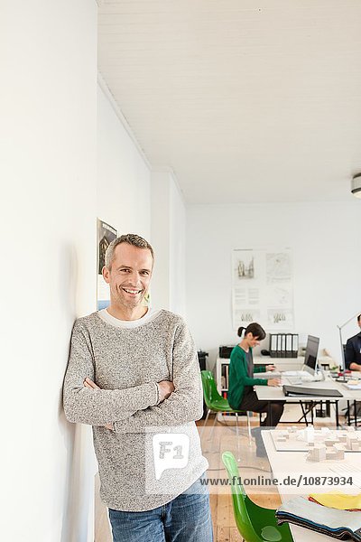 Mature man in office leaning against wall  arms crossed looking at camera smiling