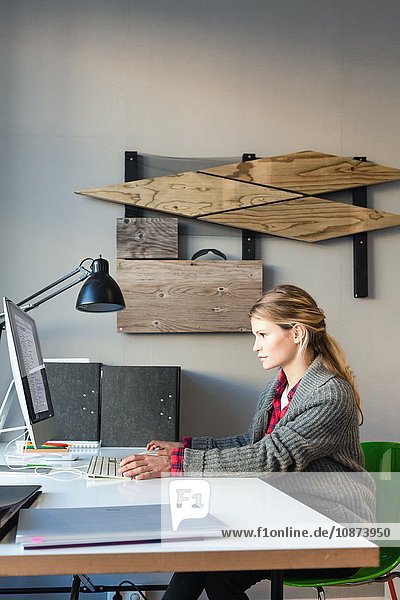 Side view of young woman in office sitting at desk using computer