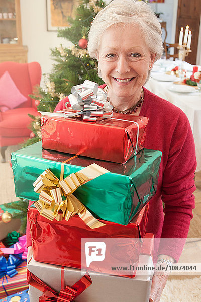 Frau hält Stapel Weihnachtsgeschenke in der Hand und schaut lächelnd in die Kamera