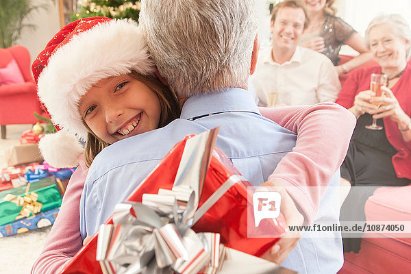 Enkelin hält Weihnachtsgeschenk und umarmt Großvater lächelnd