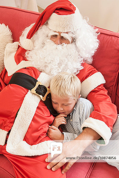 Mann sitzt als Weihnachtsmann verkleidet auf Sofa und umarmt Jungen