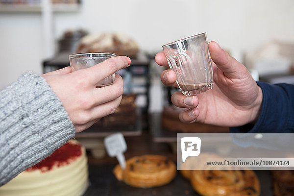 Close up of couple's hands raising an espresso toast in cafe