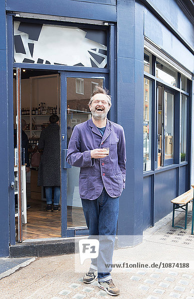 Porträt eines männlichen Cafébesitzers  der auf der Straße lacht und Espresso trinkt