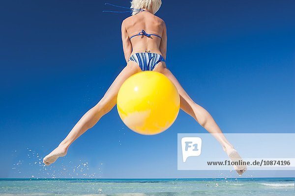 Rückansicht einer jungen Frau  die auf einem Raumtrichter am Strand in die Luft springt  Mallorca  Spanien
