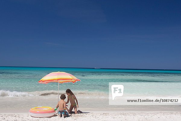 Mädchen und Bruder spielen unter einem Sonnenschirm am Strand  Mallorca  Spanien