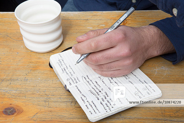 Hand eines Mannes am Cafétisch schreibt in Notizbuch