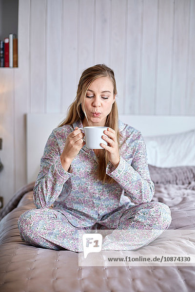 Frau im Pyjama trinkt Kaffee im Bett