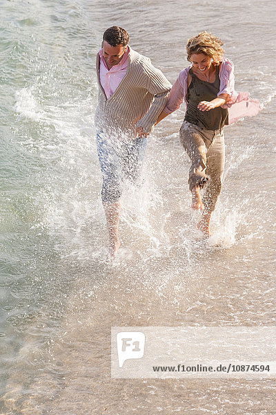 Happy mature couple running and splashing in sea  Majorca  Spain