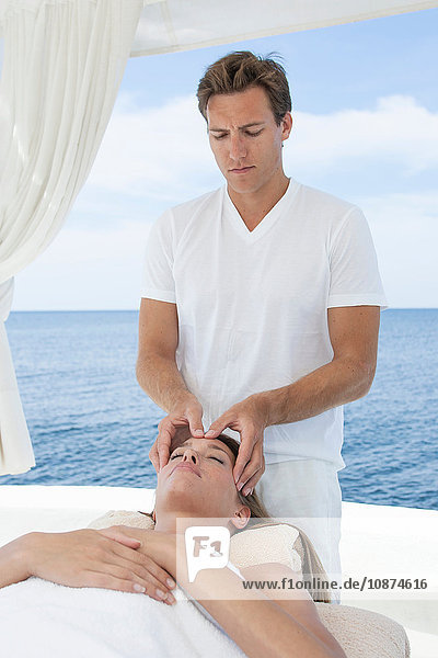 Male masseur giving young woman a head massage at beach resort  Majorca  Spain