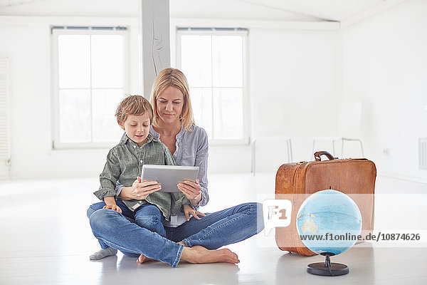 Mature woman and son sitting on floor looking at digital tablet