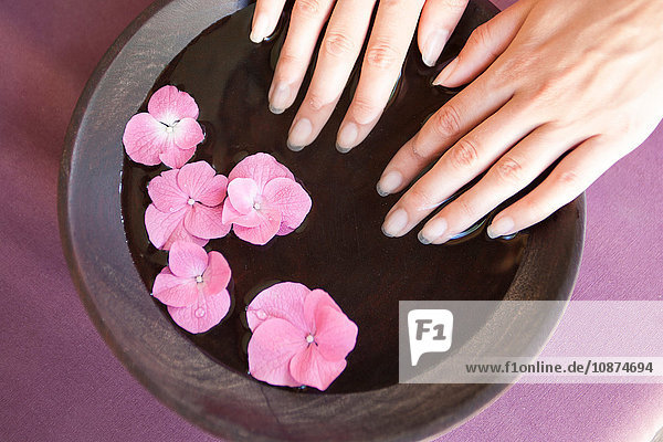 Young woman's fingernails soaking in bowl of pink flower petal water at spa