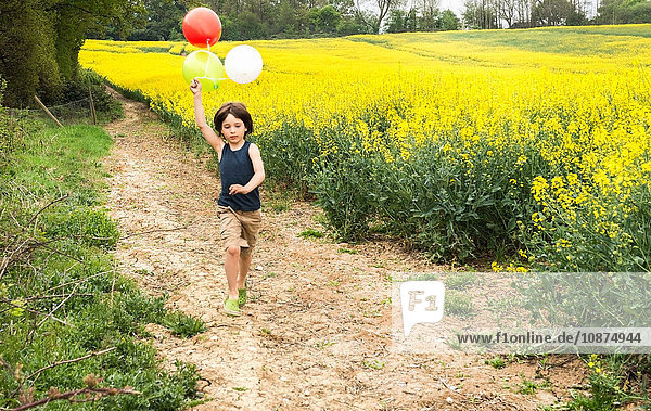 Junge läuft auf gelber Blumenfeldbahn und zieht Luftballons