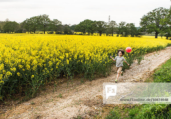Junge läuft auf gelber Blumenfeldbahn und zieht roten Ballon