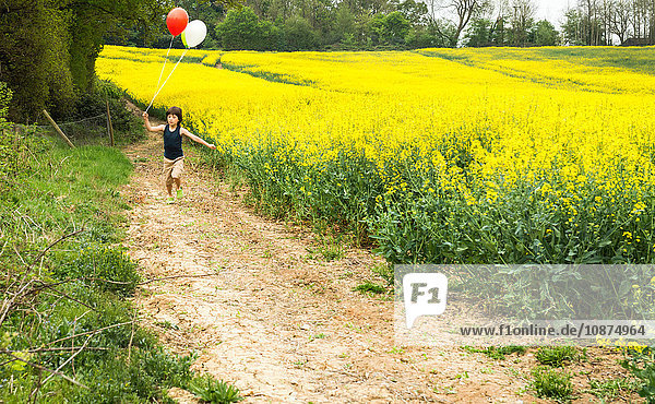 Junge rennt entlang der gelben Blumenfeldbahn und zieht rote und weiße Luftballons