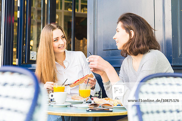 Two young women eating breakfast at sidewalk cafe Paris France