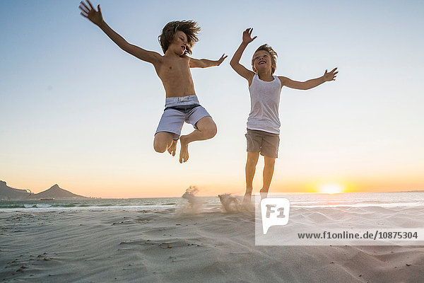 Brothers on beach jumping in mid air at sunset