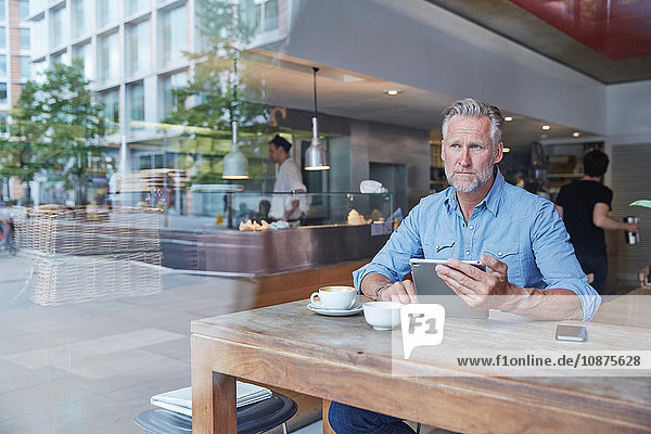 Reifer Mann sitzt im Café und benutzt ein digitales Tablett