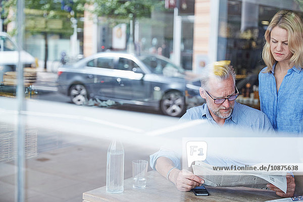 Reifer Mann und Frau im Cafe  Zeitung lesen  Straße spiegelt sich im Fenster
