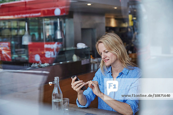 Reife Frau sitzt im Café  benutzt Smartphone  Bus spiegelt sich im Fenster