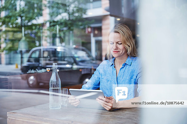 Reife Frau sitzt im Café  benutzt digitales Tablet  Taxi spiegelt sich im Fenster