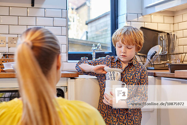 Boy carrying stack of mugs in kitchen