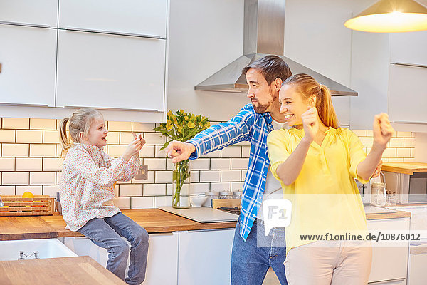 Daughter taking photograph of funny parents in kitchen