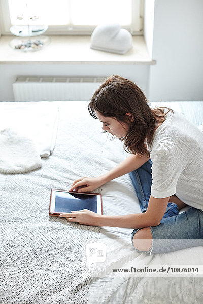 Junge Frau sitzt im Bett und liest ein digitales Tablett