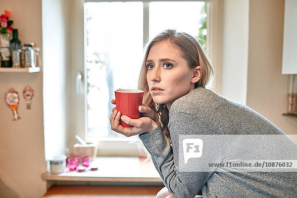 Junge Frau lehnt sich mit einer Tasse Kaffee auf dem Küchentisch vor