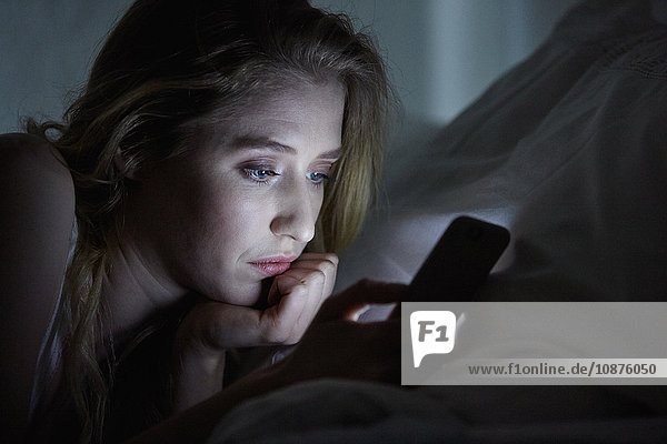 Close up of young woman lying in bed reading smartphone texts at night