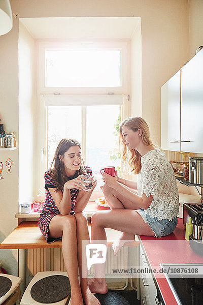 Zwei junge Frauen sitzen auf dem Küchentisch und unterhalten sich