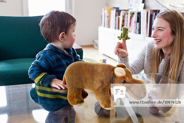 Mittlere erwachsene Frau und kleiner Sohn spielen mit Fingerpuppe im Wohnzimmer