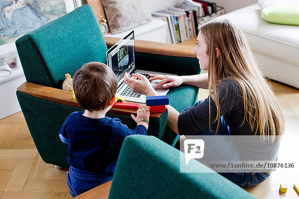 Mittelgroße erwachsene Frau und kleiner Sohn schauen auf den Laptop im Wohnzimmer