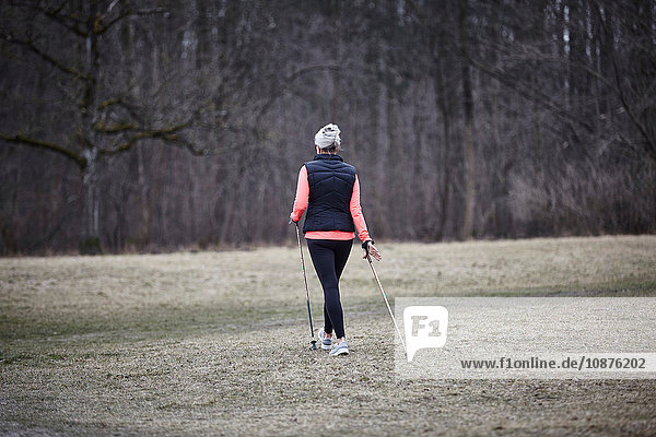 Rear view of mature female training in park  nordic walking with poles